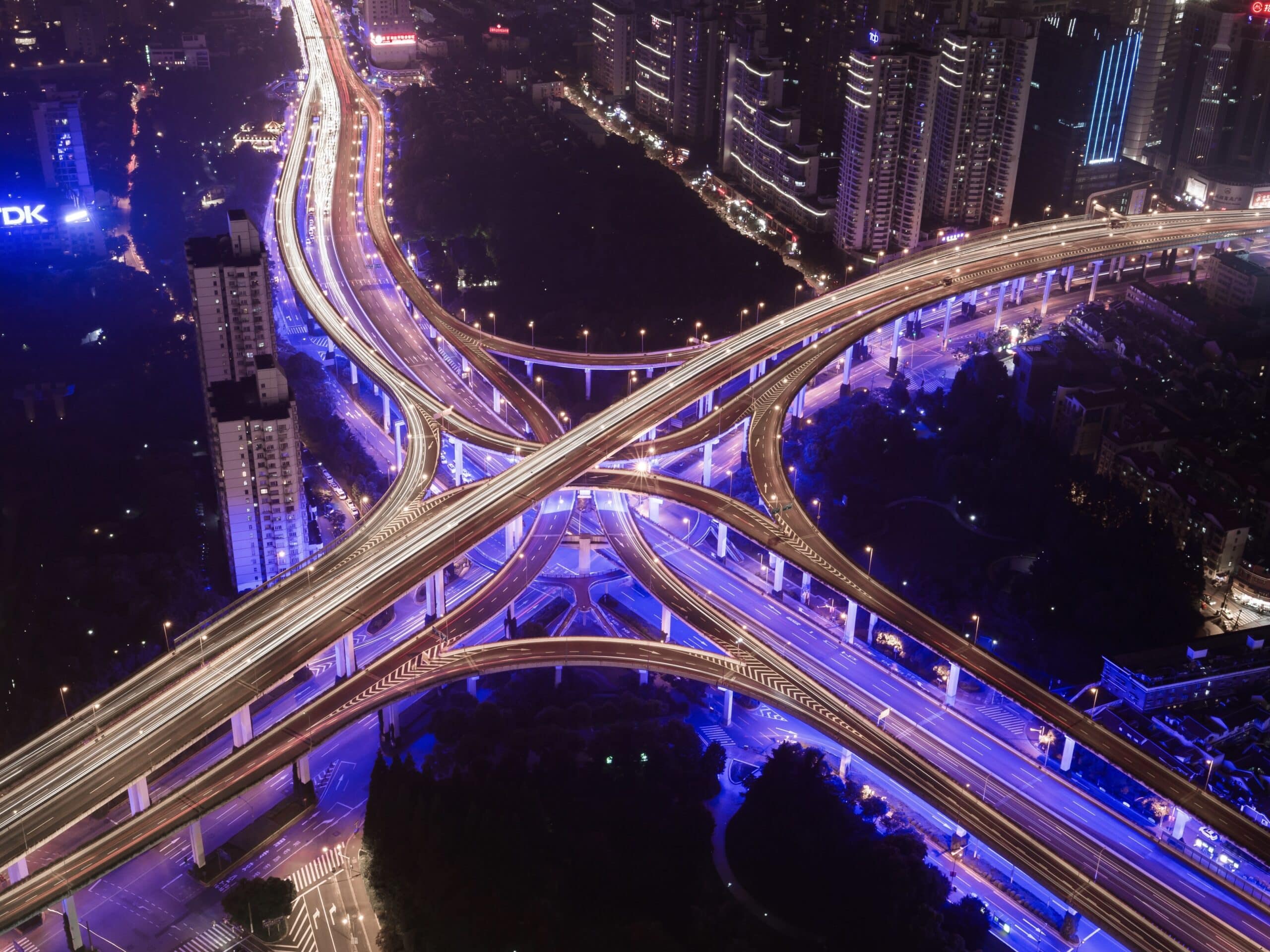 Cityscape and interchange Aus der Vogelperspektive wird ein Highway bei Nacht gezeigt. Die Lichter sind aufgrund der Geschwindigkeit verschwommen. Diese Dynamik drücken auch die Digital Business Solutions aus